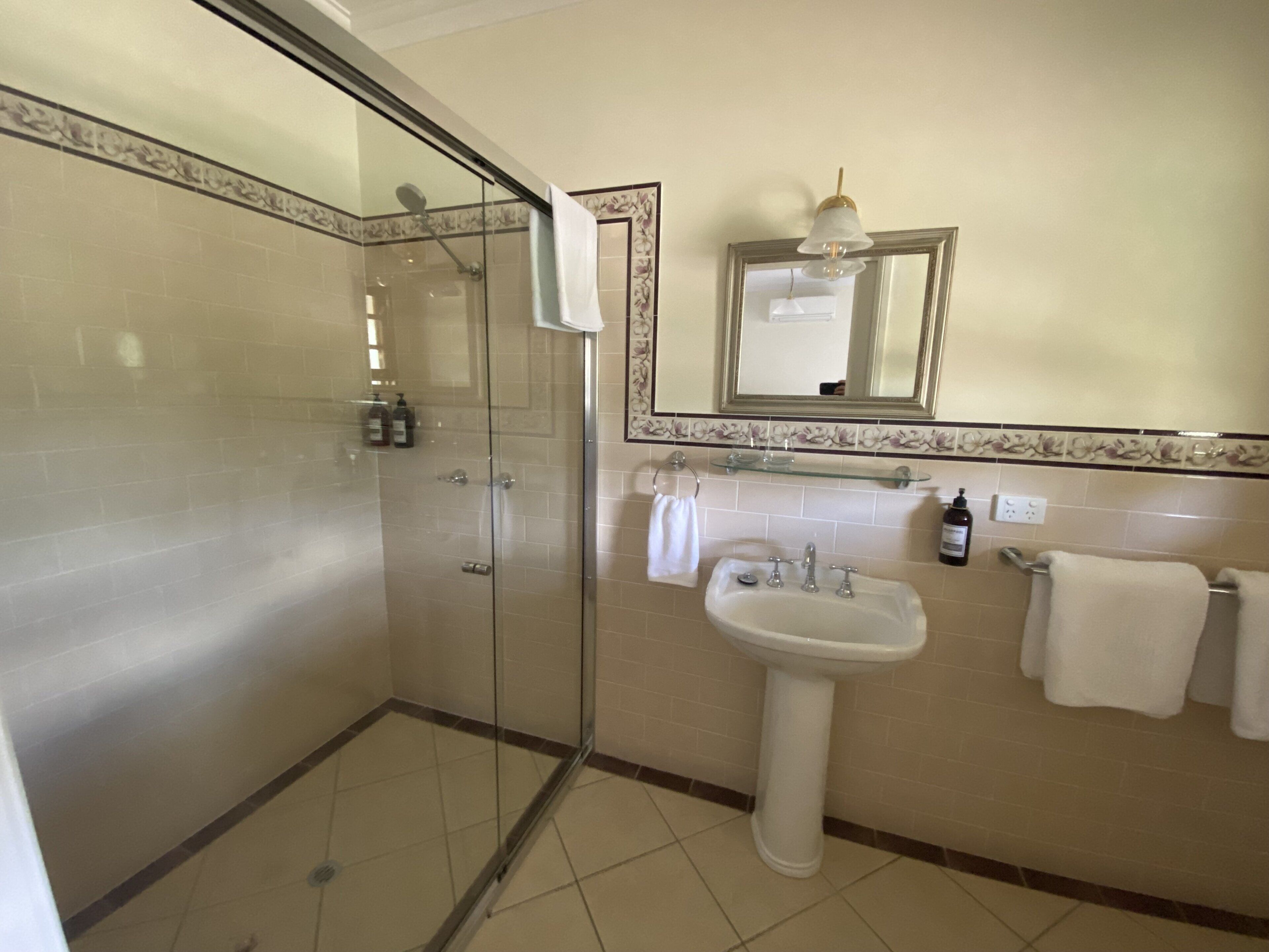 A bathroom with a glass-enclosed shower, a pedestal sink, a mirror, and a towel rack.