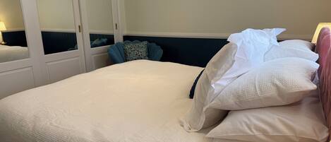 A hotel room with a large bed, a nightstand, a mirror, and a window with a view.