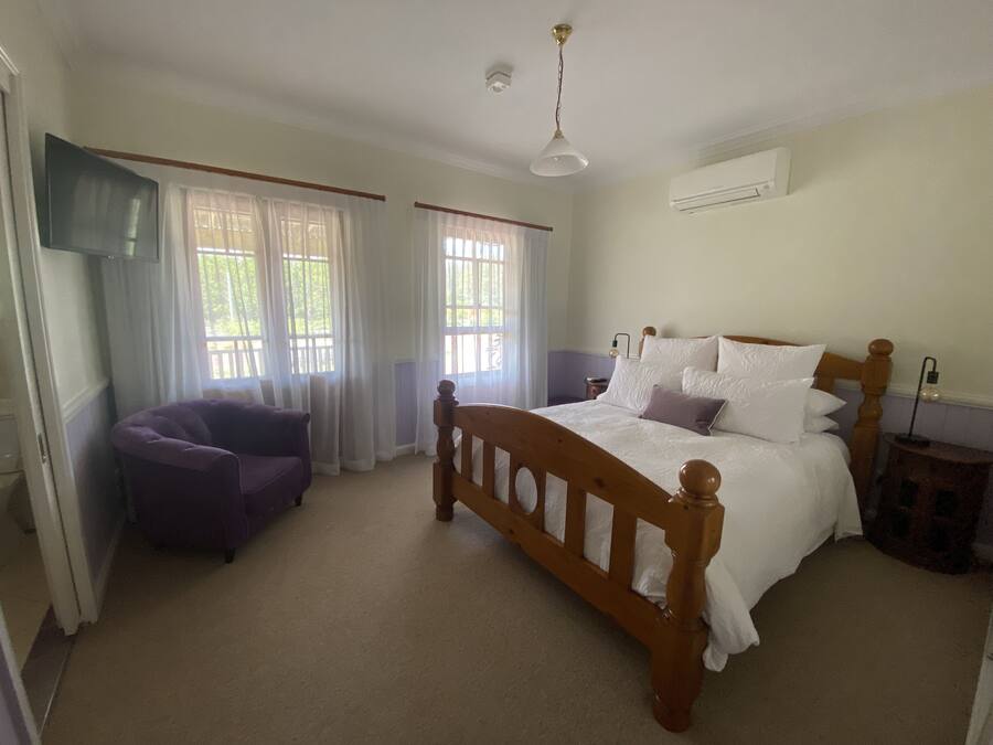 Quarto com cama de madeira, poltrona roxa e ventilador de teto.
