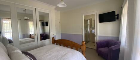 A bedroom with a bed, a wooden headboard, a purple armchair, a television, and a bathroom door.