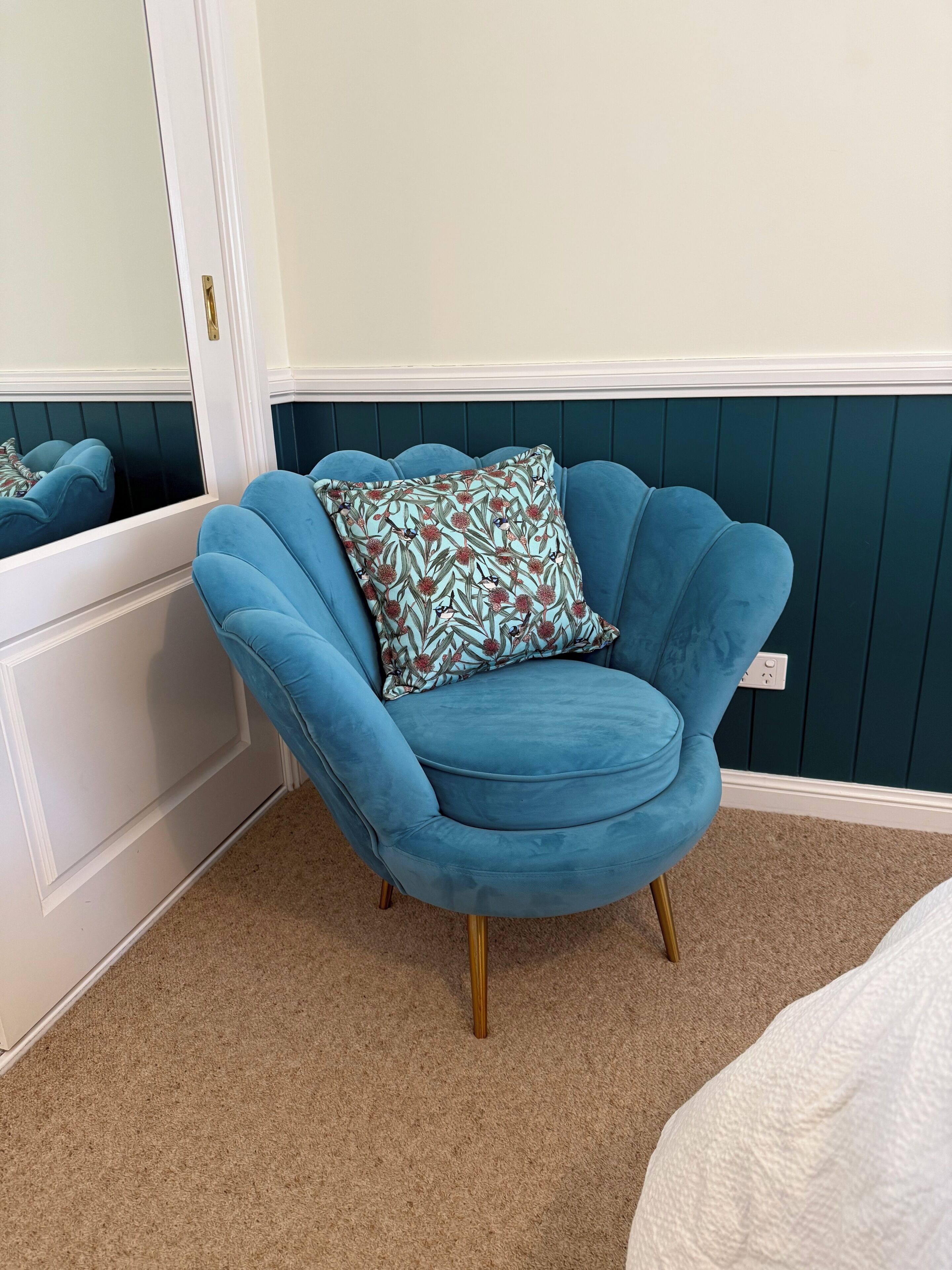 A corner room with a blue armchair, a patterned pillow, a white door, and a dark green wall.