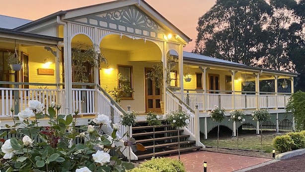 Una casa de dos pisos con porche, escalones y un jardín de rosas blancas.