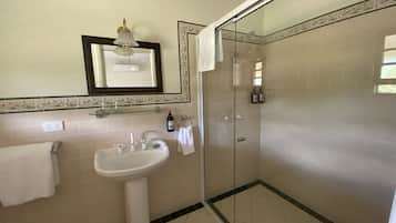 Un baño con lavamanos pedestal, ducha con mampara de vidrio y espejo con marco decorativo.
