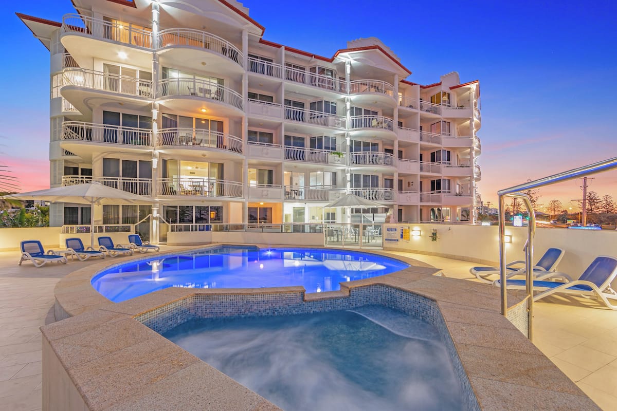 Un hotel de varios pisos con piscina, mobiliario exterior y balcones.