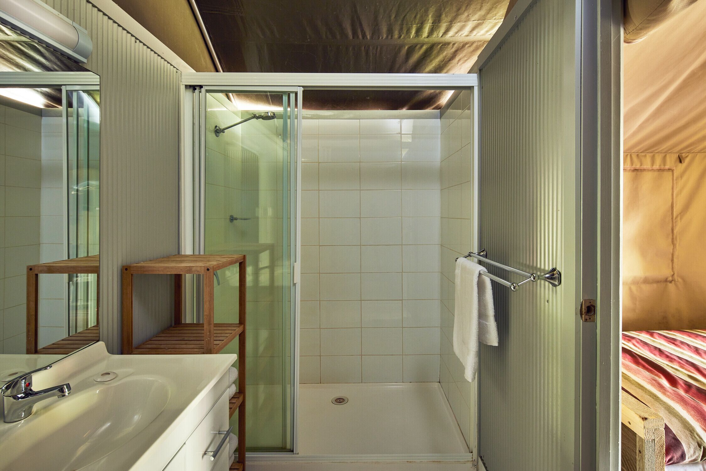Un baño con ducha de vidrio, un taburete de madera, un lavamanos y un perchero para toallas.