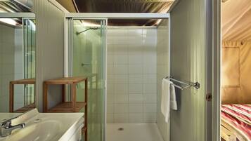 A bathroom with a glass-enclosed shower, a wooden stool, a sink, and a towel rack.