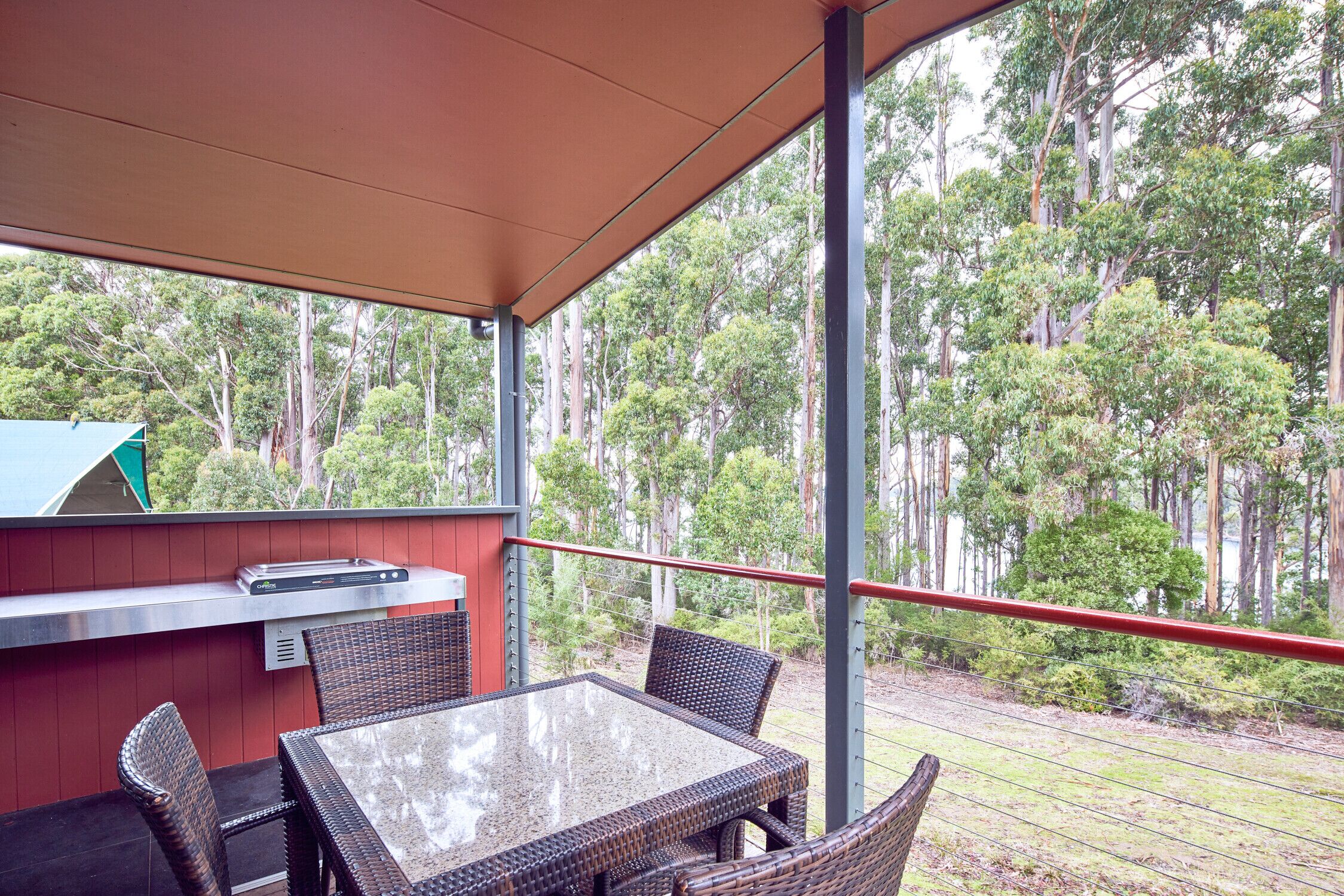An outdoor patio with a glass table and wicker chairs, overlooking a forested area.