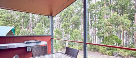 Un patio al aire libre con una mesa de vidrio y sillas de mimbre, con vistas a una zona boscosa.