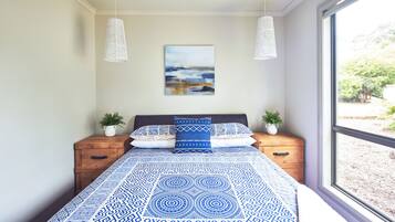 A bedroom with a bed, two bedside tables, a window, and a wall-mounted painting.