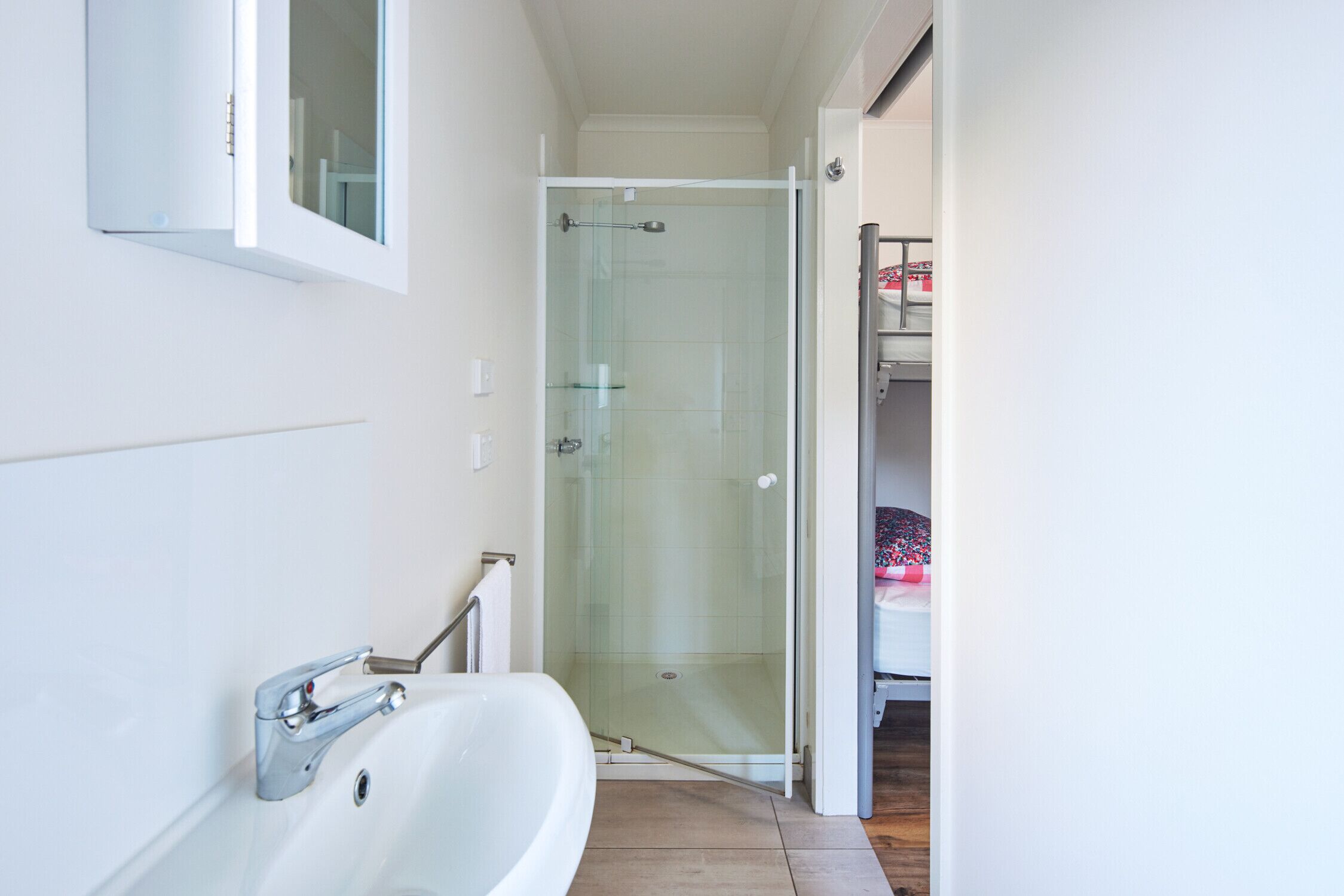 A bathroom with a white bathtub, a glass-enclosed shower, and a visible bed in the adjacent room.