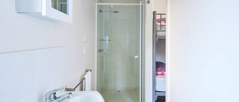 A bathroom with a white bathtub, a glass-enclosed shower, and a visible bed in the adjacent room.