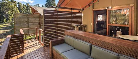 Una terraza de madera con zona de estar y equipo para hacer parrilladas.