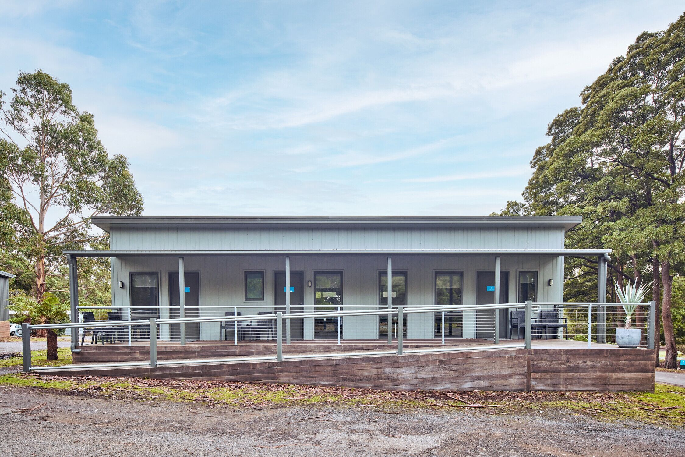A modern building with a flat roof, large windows, and a covered outdoor area with a railing.