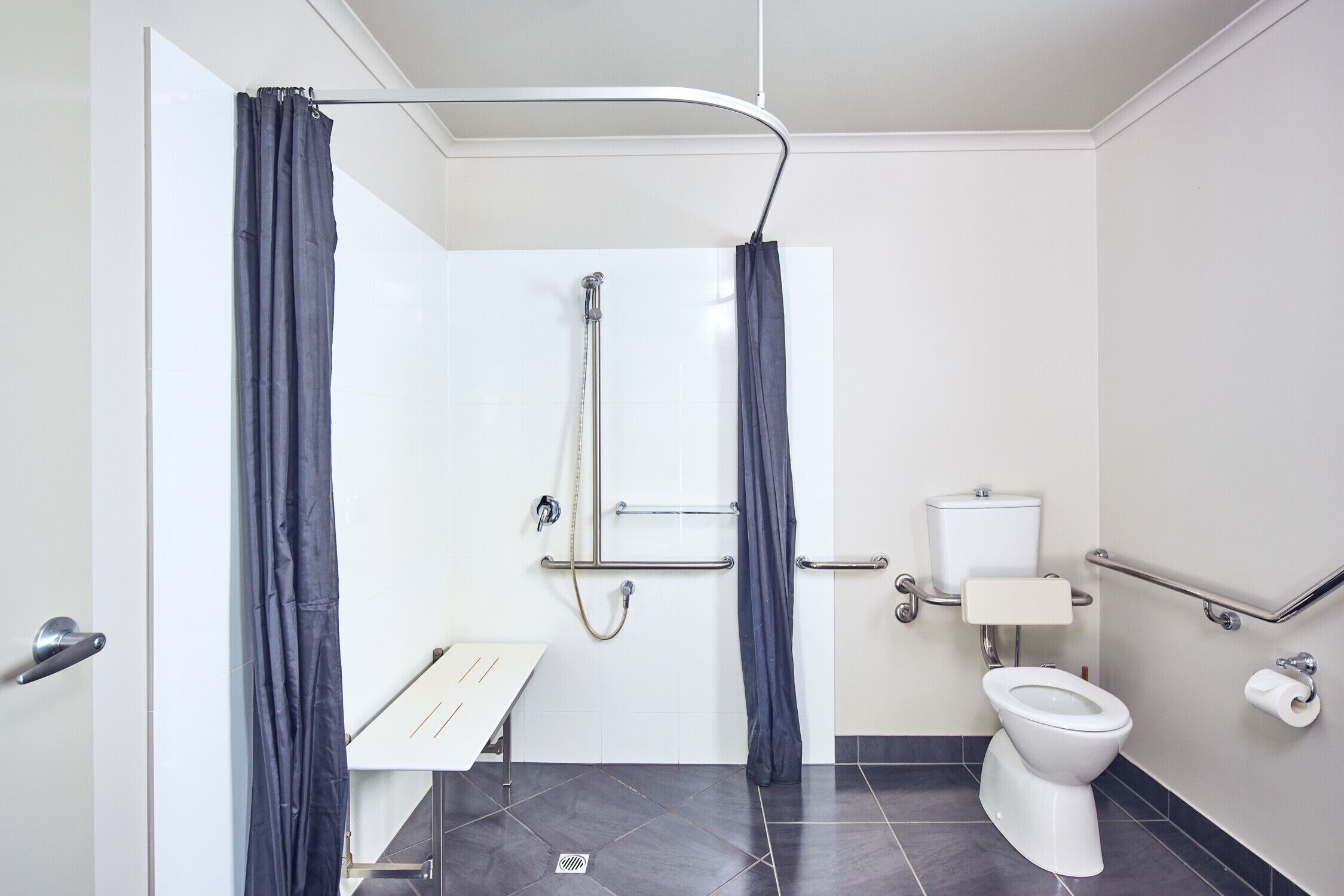Un baño moderno con ducha, inodoro y barras de apoyo.