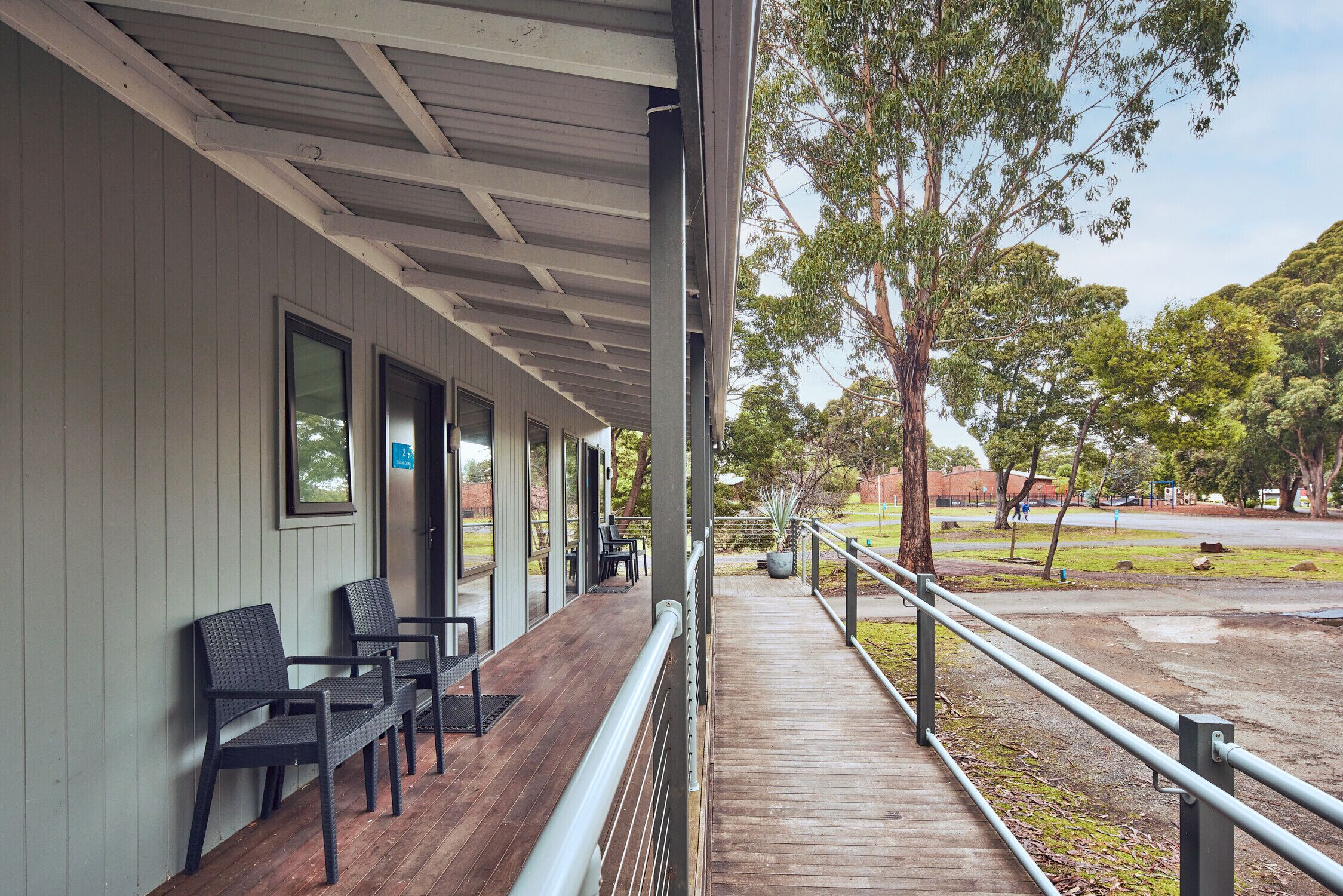 A covered outdoor area with wooden flooring, metal railings, and black chairs.