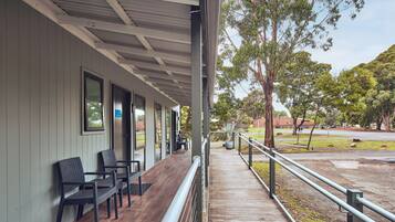 A covered outdoor area with wooden flooring, metal railings, and black chairs.