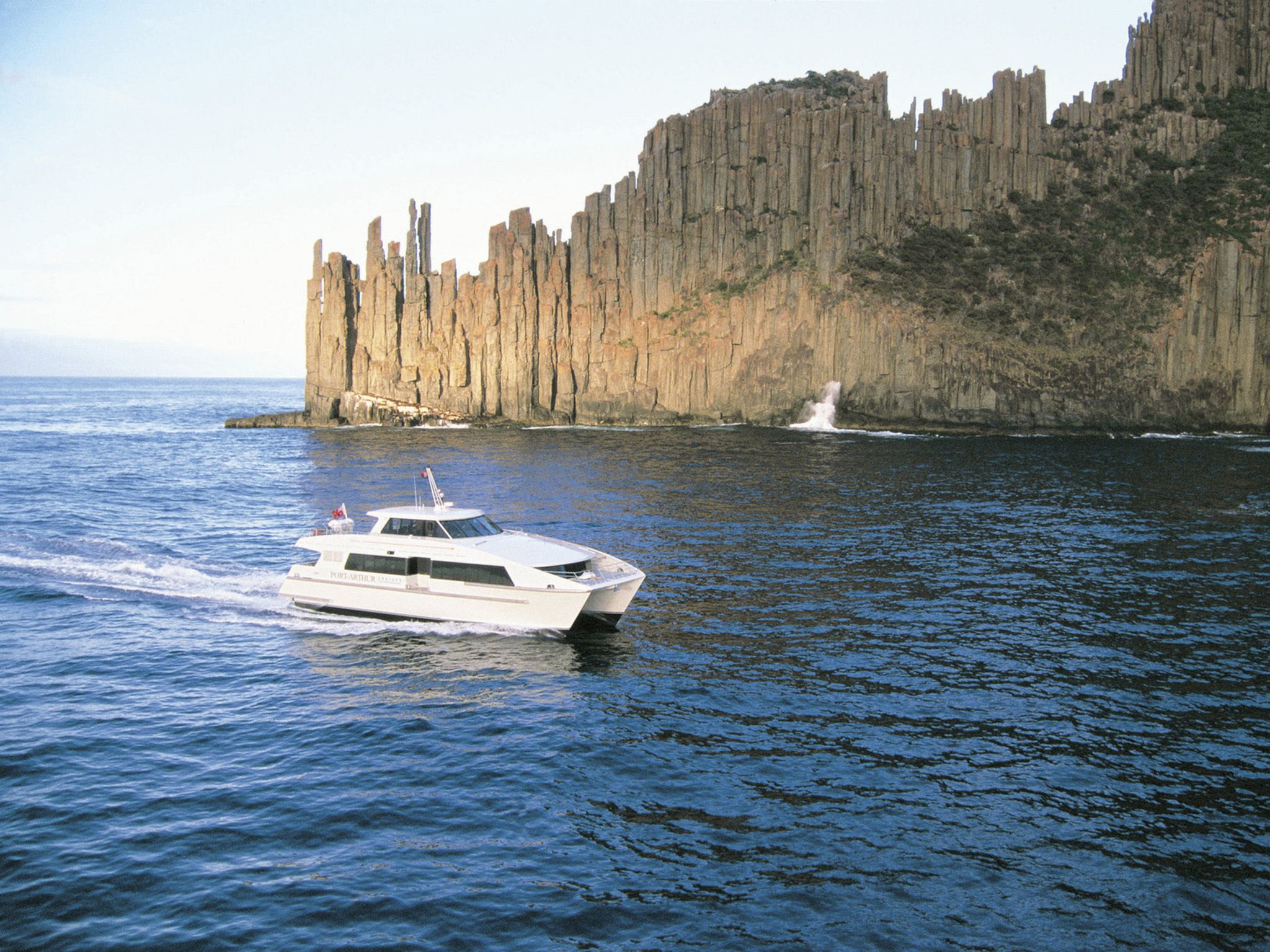 A white boat on calm water near a rocky cliff.