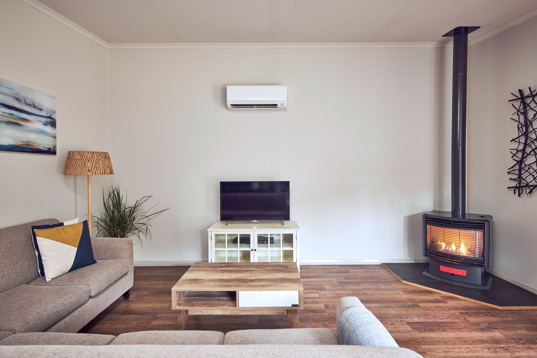 A living room with a sofa, a coffee table, a TV, a white cabinet, a plant, and a wood-burning stove.