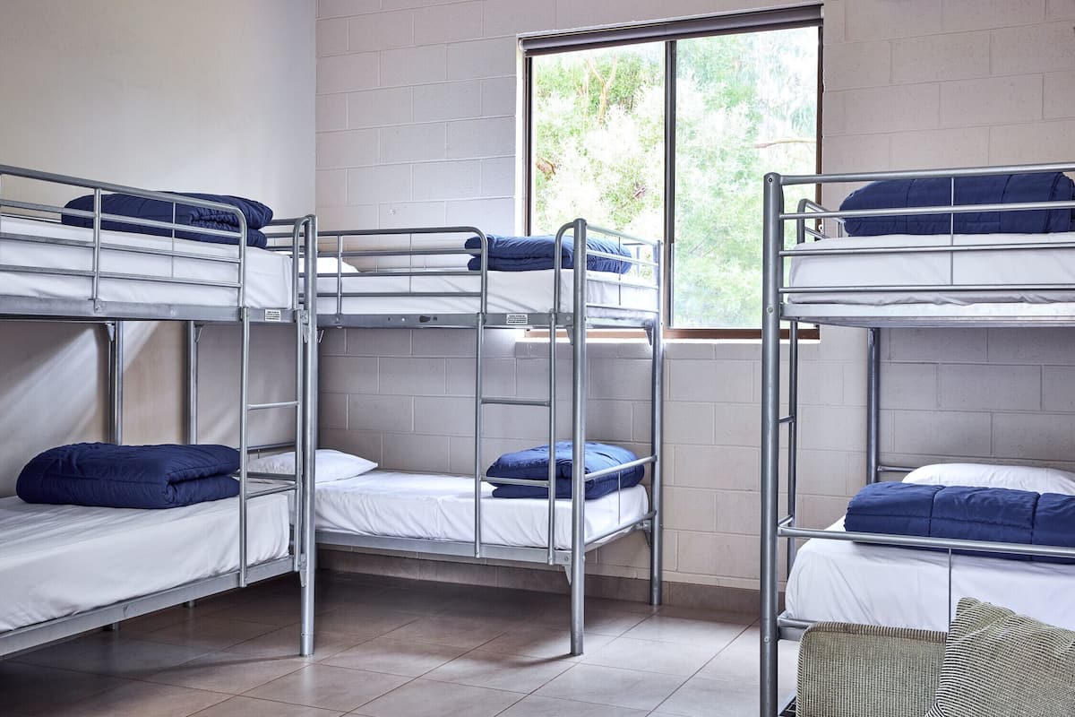 Ein Schlafsaalzimmer mit Etagenbetten, einem Fenster mit Blick auf Grünflächen und Fliesenboden.