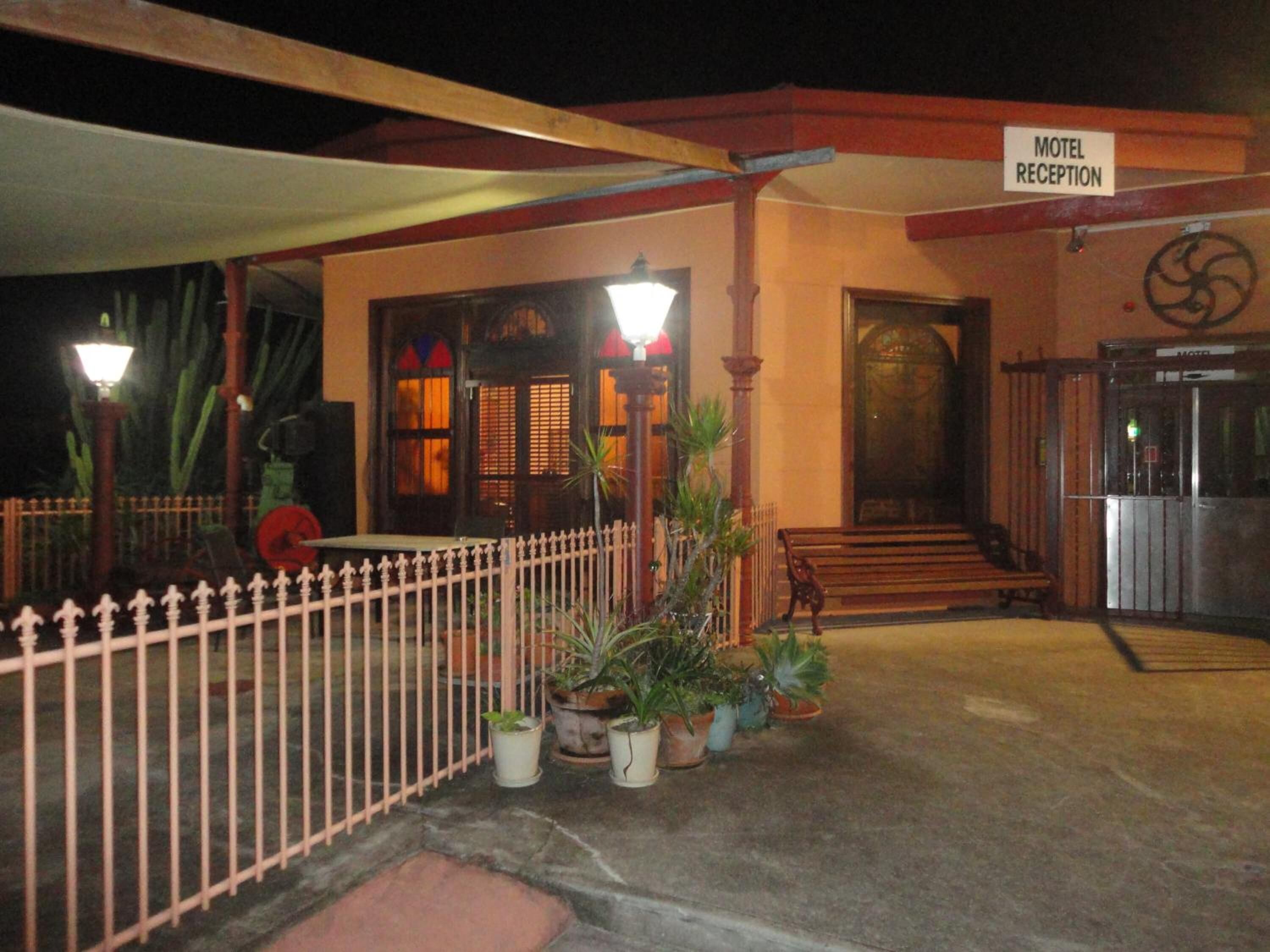 A motel reception with a sign, a wooden fence, potted plants, and a staircase leading to the entrance.