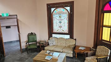 A room with a green armchair, a patterned sofa, a wooden coffee table, and a stained glass window.