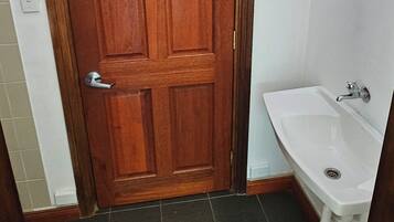 Un baño con puerta de madera, lavamanos blanco y ventana sobre la puerta.