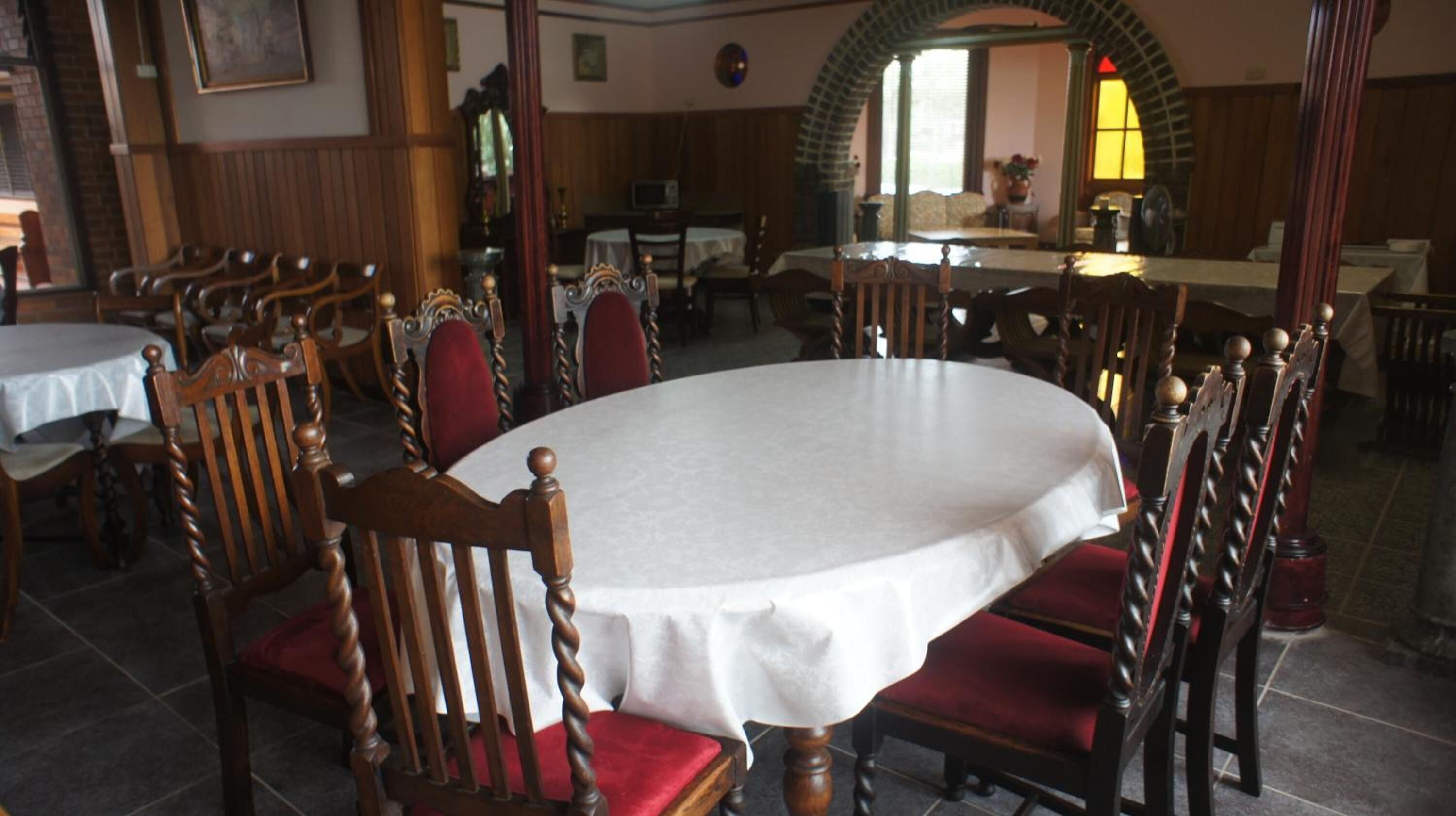 A dining area with round tables and wooden chairs, a TV in the background, and a stained glass window.