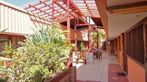 A covered outdoor area with a tiled floor, wooden benches, and potted plants. - A Railway Lodge (Taree)