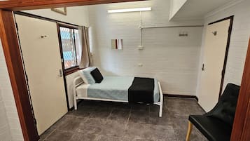 Ett litet, kompakt rum med en säng, en stol och ett fönster med gardiner.