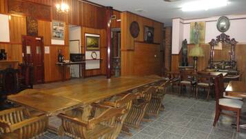 A dining area with a long wooden table and chairs, a kitchen area with a stove and refrigerator, and a tiled floor.