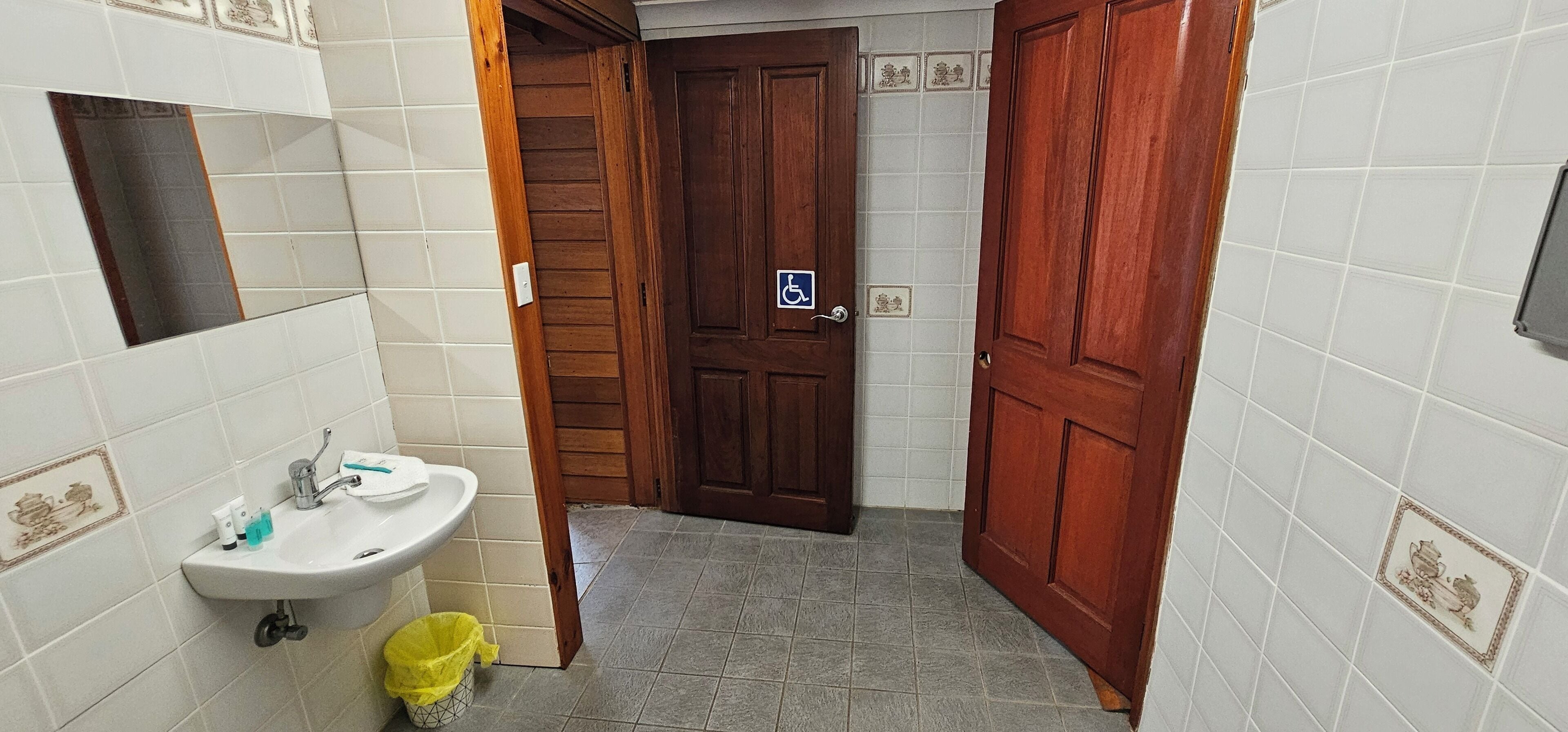 Casa de banho estreita com lavatório, espelho e porta de madeira.