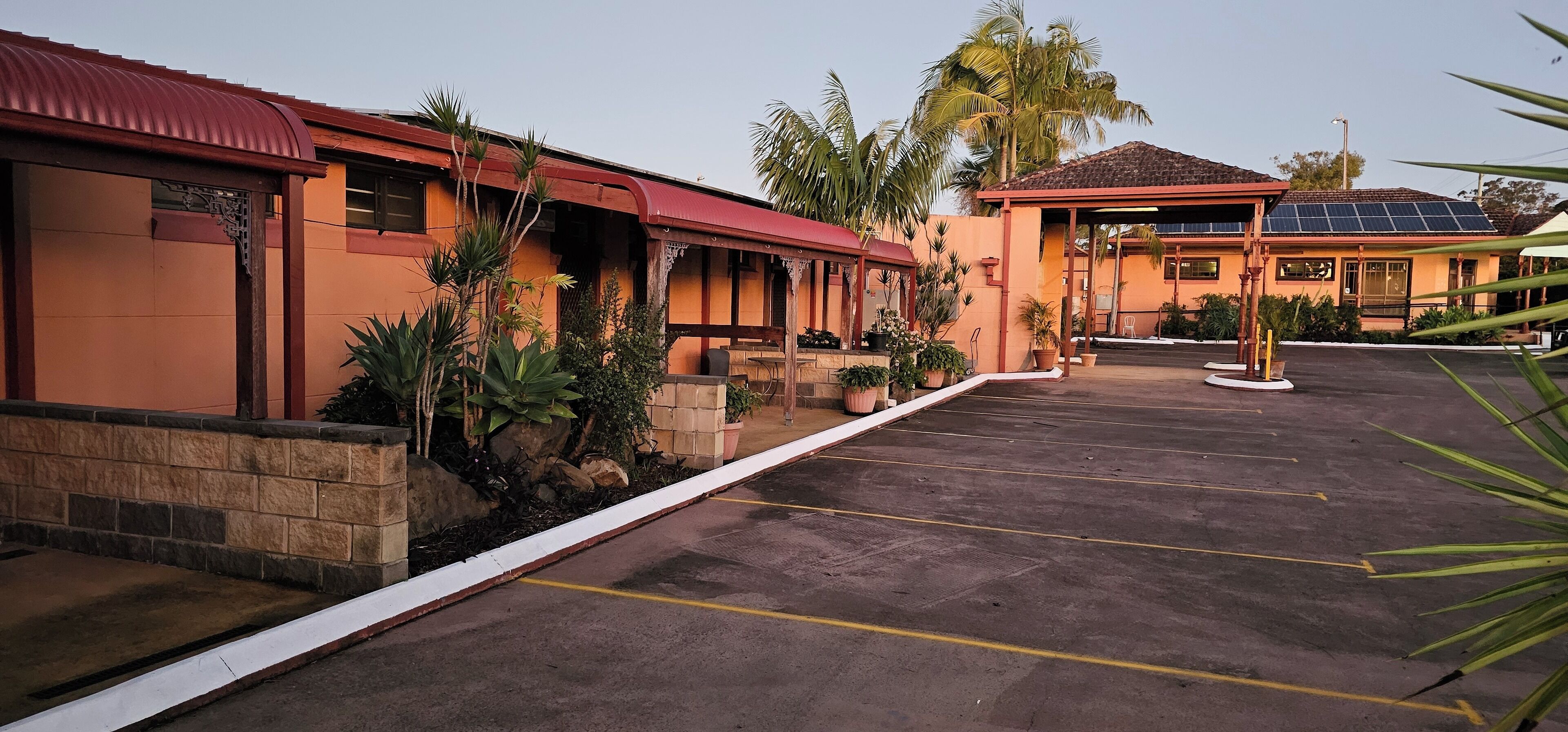 A hotel with a red roof, a covered outdoor seating area, and a parking lot with marked spaces.