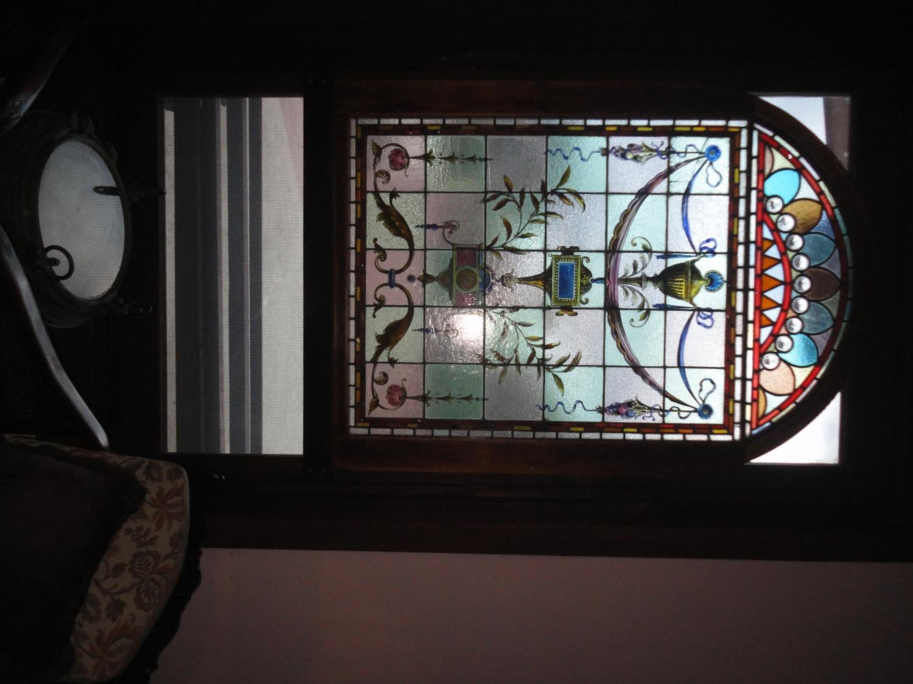 Une fenêtre à vitraux ornée de motifs floraux et géométriques, une horloge et un fauteuil à motifs.