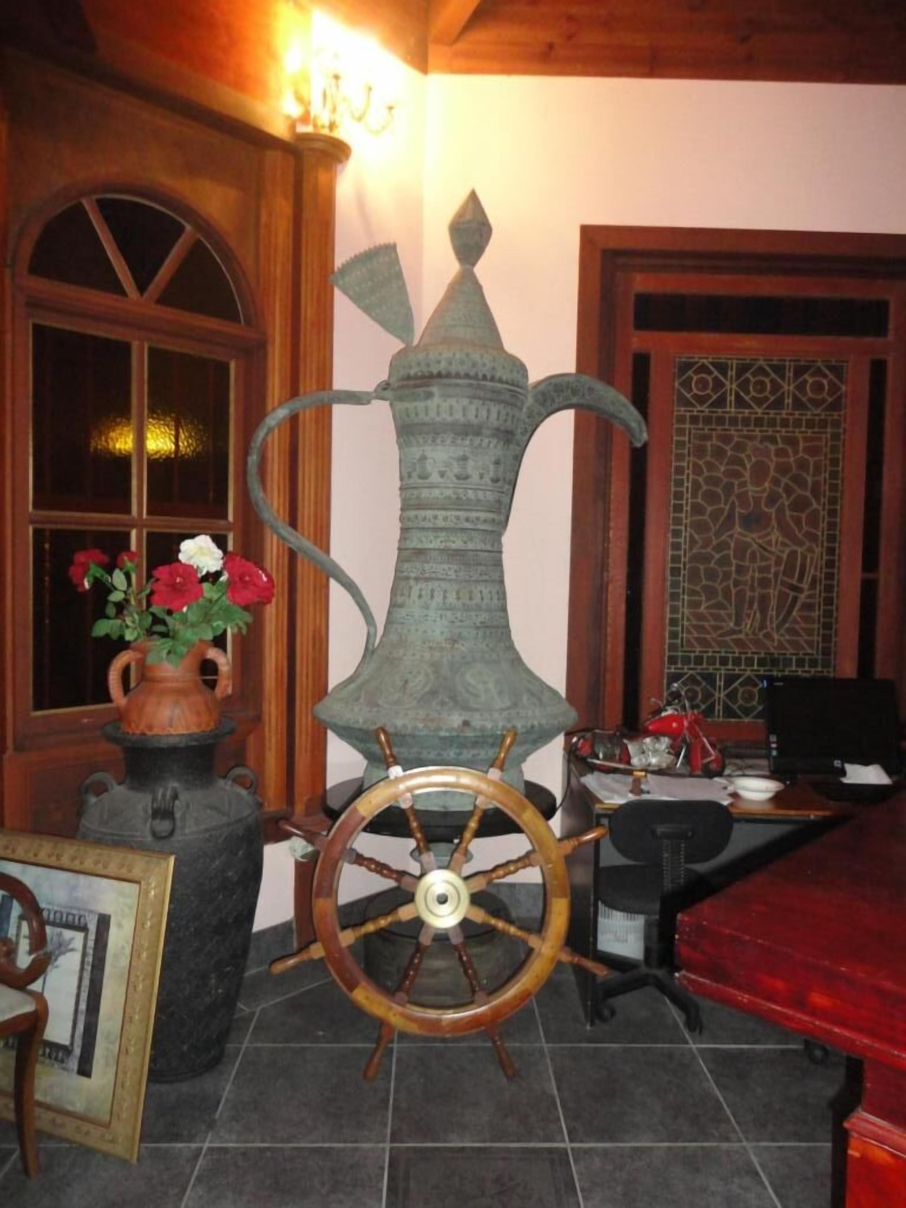 Ein Zimmer mit einer großen Dekorationsvase, einem hölzernen Steuerrad und einer Vase mit roten Blumen auf einem Tisch.