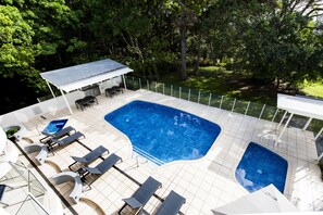 A rooftop pool with lounge chairs and a covered seating area, surrounded by trees. - Sandcastles Noosa (Noosa Heads)