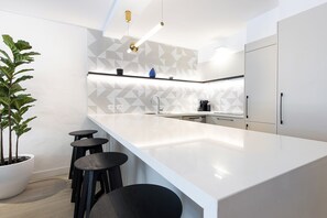 A modern kitchen with a white countertop, black stools, and a potted plant. - Sandcastles Noosa (Noosa Heads)