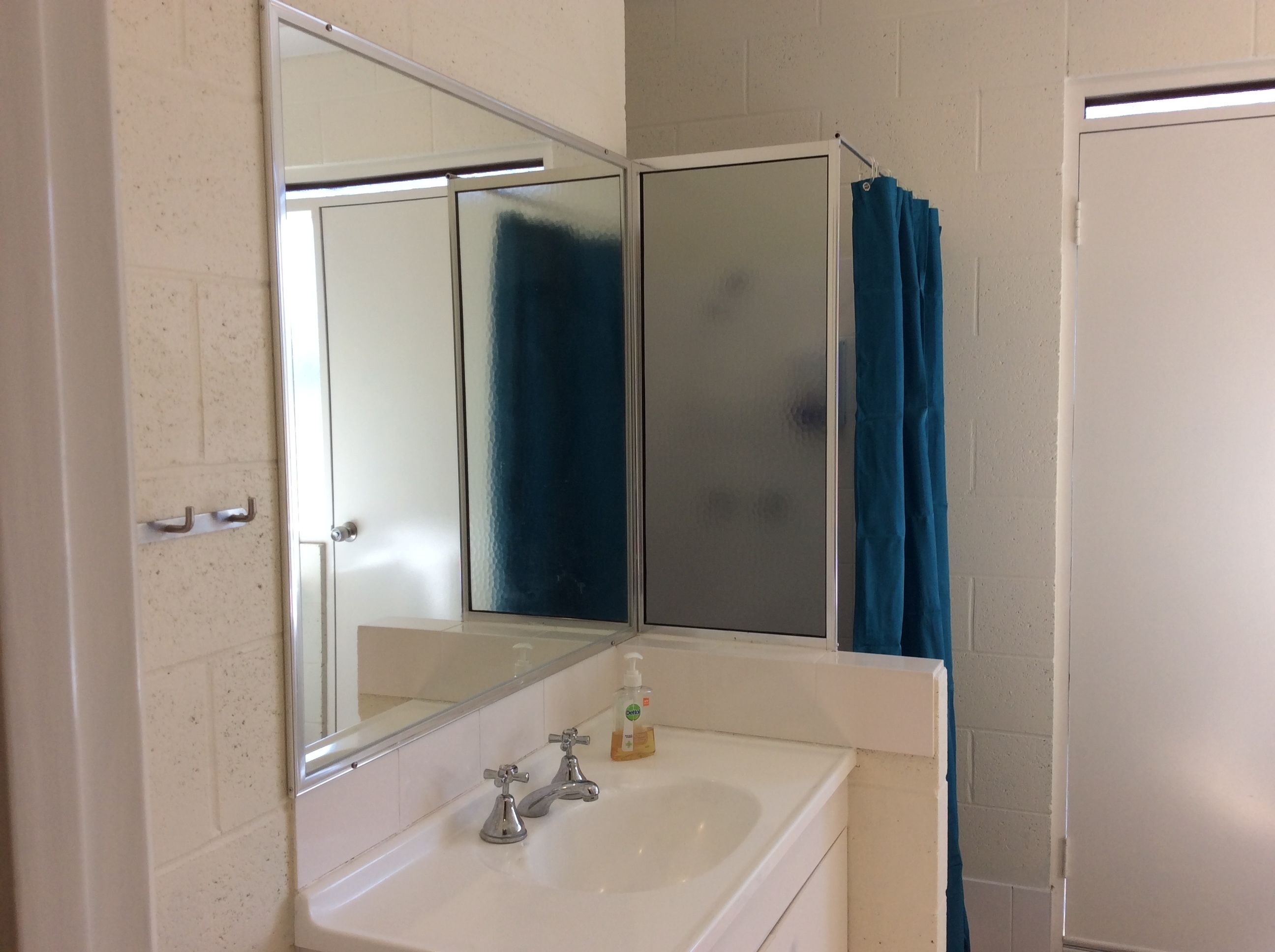 A bathroom with a white sink, two faucets, a mirror, and a blue shower curtain.