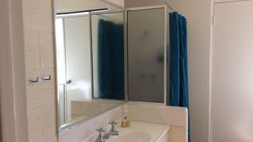 A bathroom with a white sink, two faucets, a mirror, and a blue shower curtain.