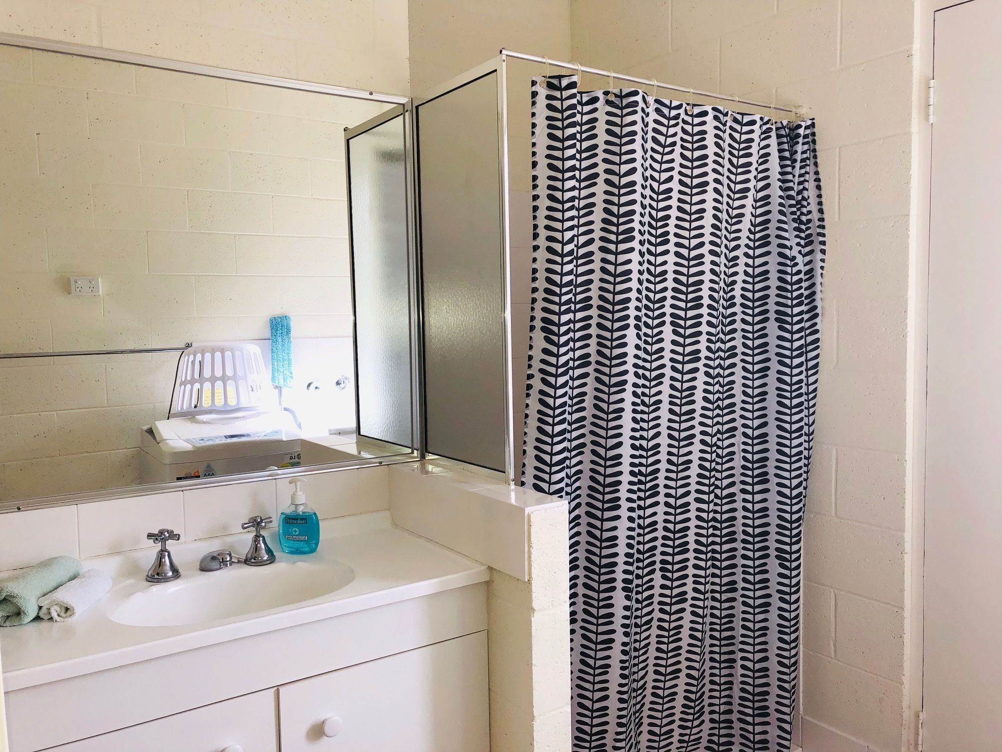 A bathroom with a white sink, two faucets, a mirror, and a shower curtain with a leaf pattern.
