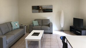 Una sala de estar con un sofá gris, una mesa de centro blanca, un mueble para televisor y un ventilador de techo.