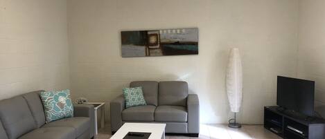 A living room with a grey sofa, a white coffee table, a TV stand, and a ceiling fan.