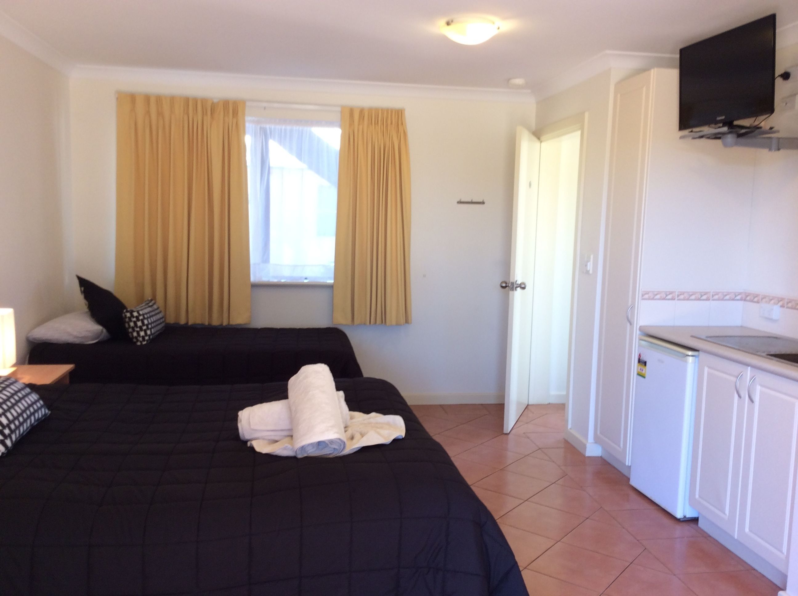 Habitación de hotel con dos camas, una ventana con cortinas, un televisor montado en la pared y una kitchenette.