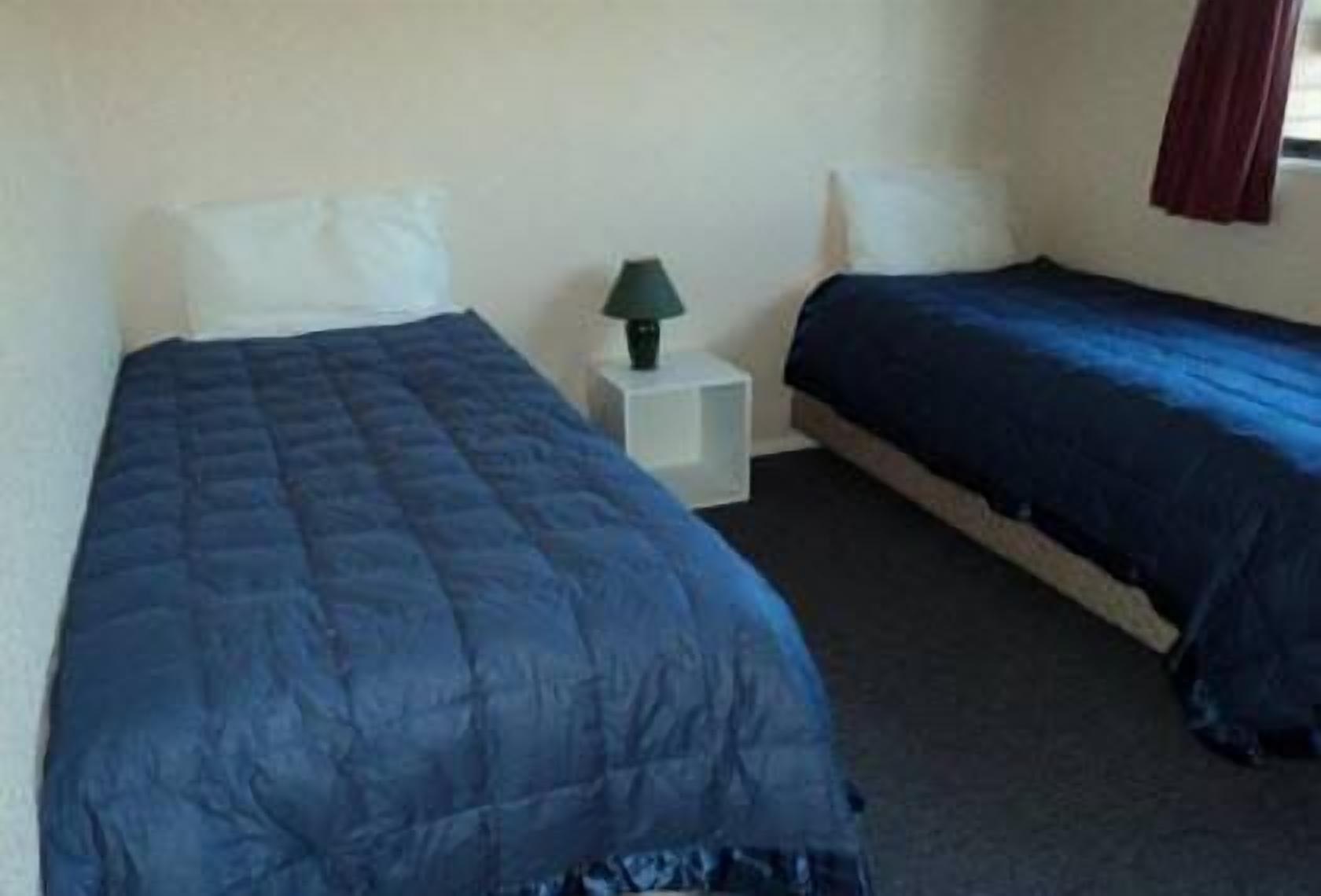 A room with two single beds, a bedside table with a lamp, and a window with curtains.