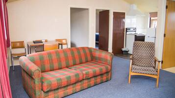 A room with a checkered sofa, a patterned armchair, a small table, and a kitchenette in the background.