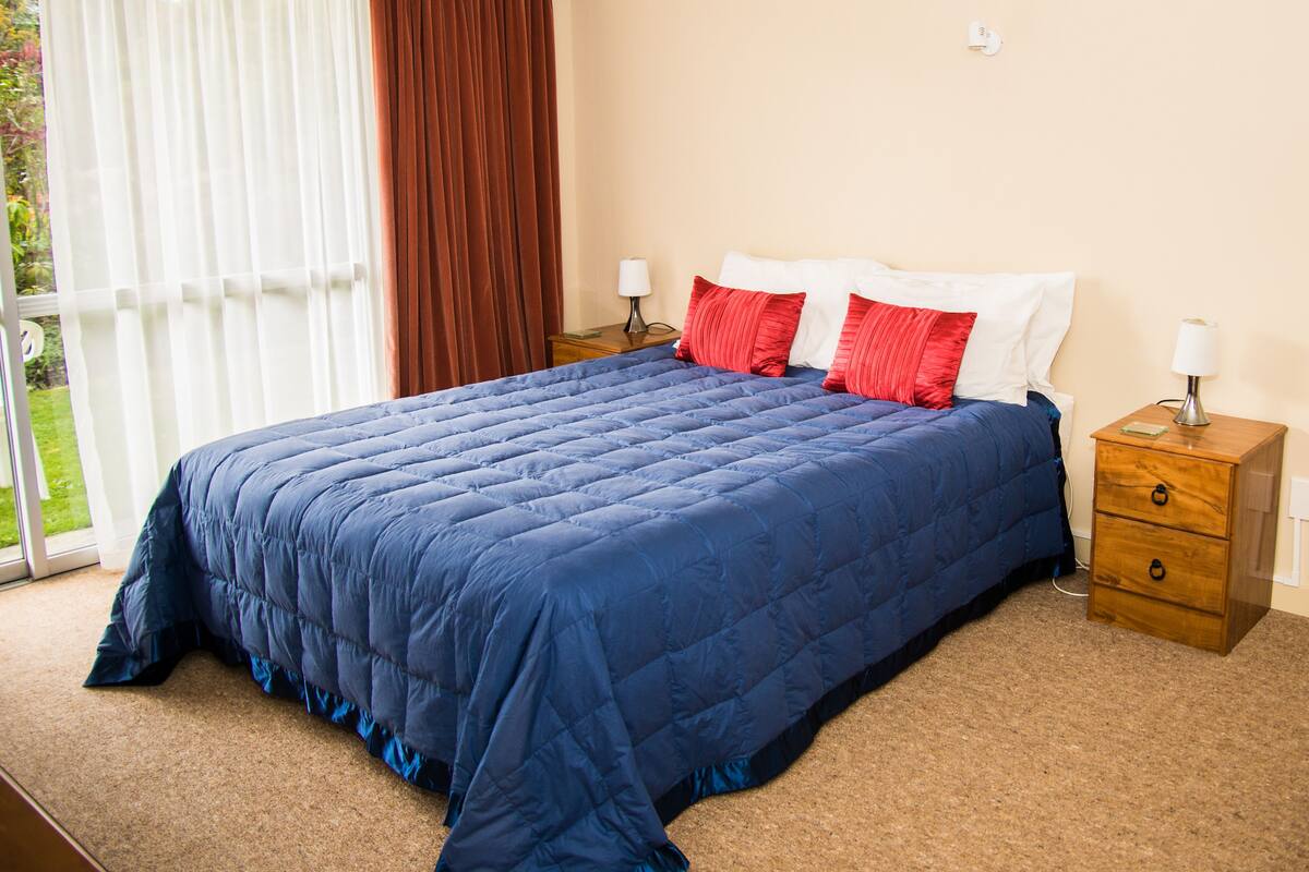 A bedroom with a large bed, two bedside tables, and a window with curtains.