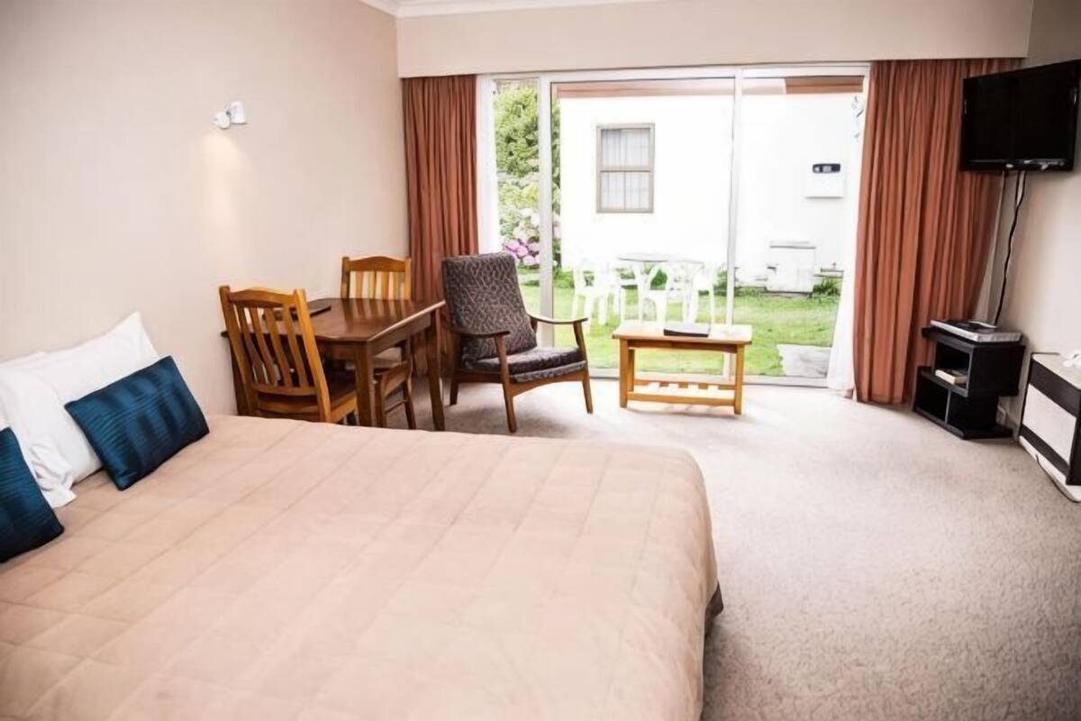 A hotel room with a bed, a table, two chairs, a TV, and a sliding glass door to the outside.
