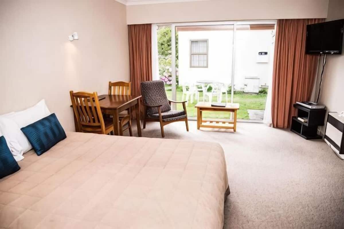 Habitación de hotel con cama, una mesa, dos sillas, televisión y puerta corrediza de vidrio al exterior.