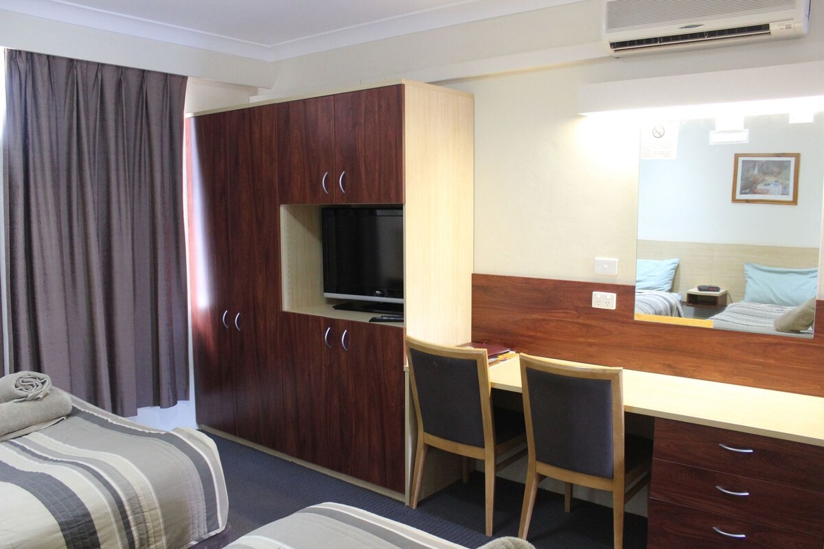 A compact hotel room with a bed, a desk with two chairs, a TV, a mirror, and a wardrobe.