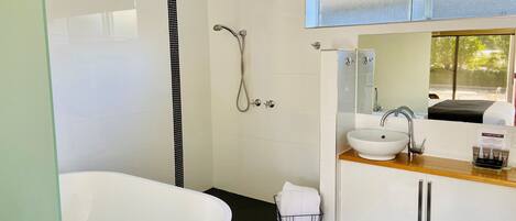 A modern bathroom with a large bathtub, a shower, a sink, and a vanity with cabinets.