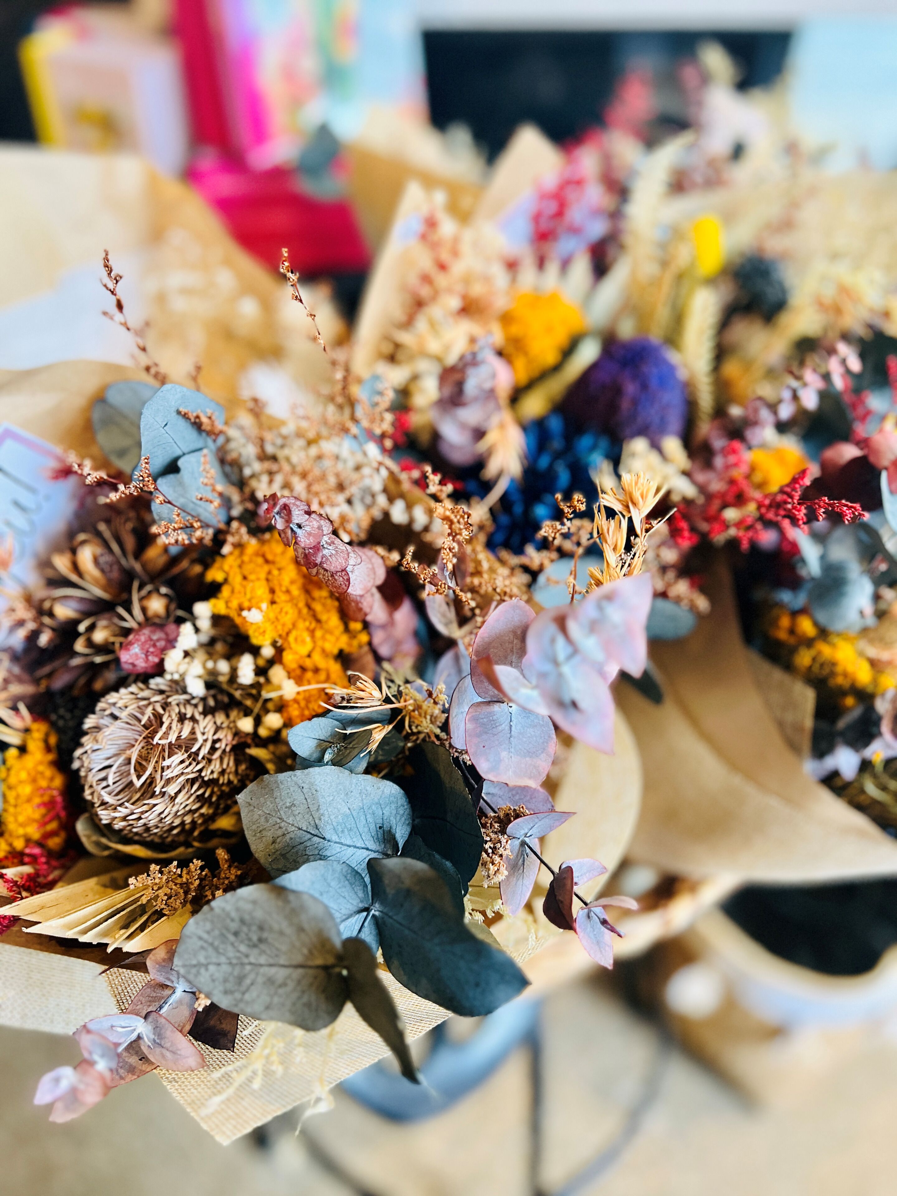 Un ramo de flores con diversas follajes y elementos secos, dispuesto en un recipiente.